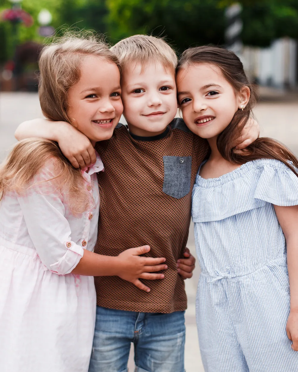 Three smiling children standing together outdoors