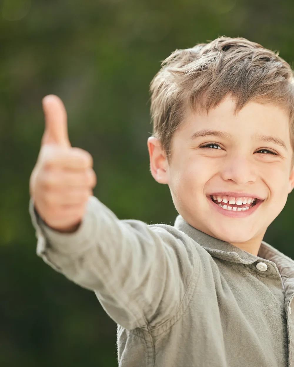 Smiling boy giving a thumbs-up outdoors