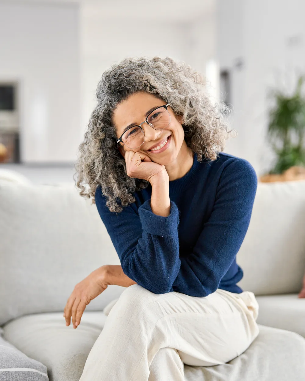 Smiling woman seated on a sofa with her hand near her face